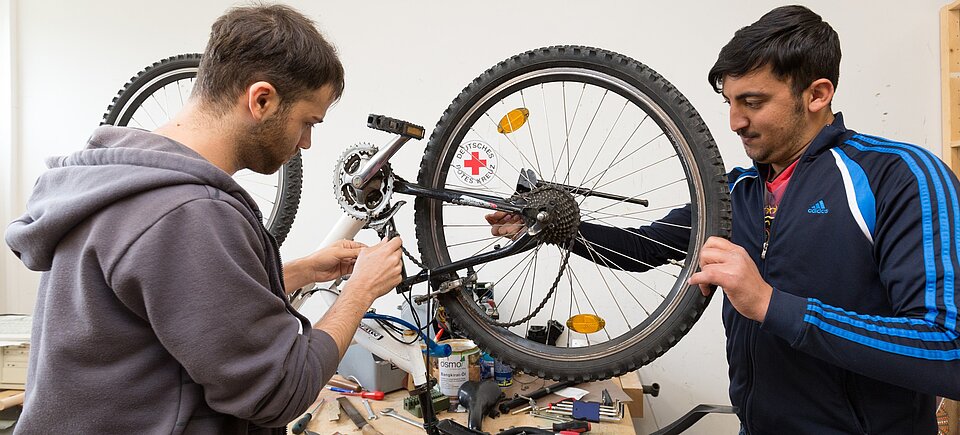 Zwei Personen, davon ein geflüchteter Menschen, reparieren ein Fahrrad