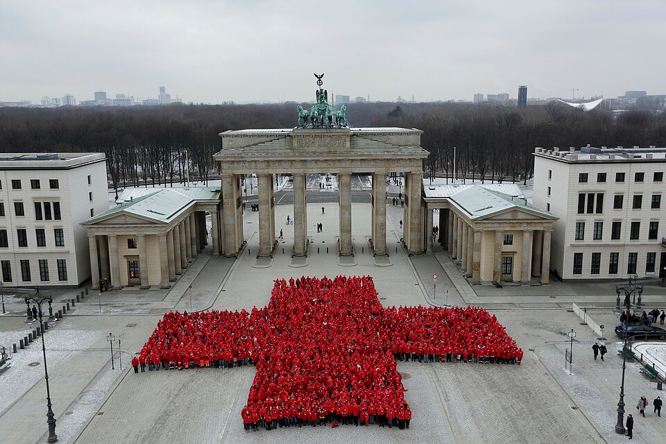 Viele Menschen in roten Jacken bilden vor dem Brandenburger Tor ein großes Rotes Kreuz