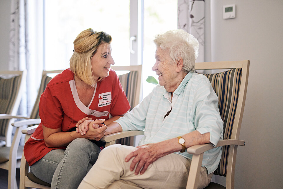 Eine Pflegemitarbeiterin des DRK sitzt bei einer zu pflegenden Person und wendet sich ihr zu.
