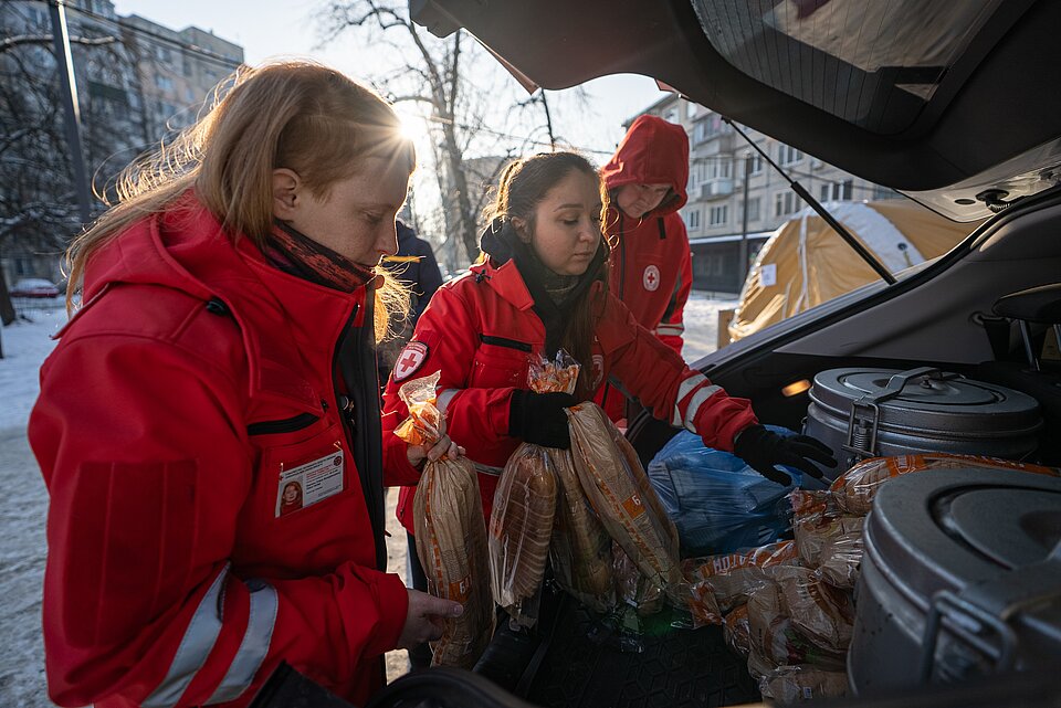 Menschen mit roten Jacken vom Ukrainischen Roten Kreuz laden Lebensmittel aus dem Kofferraum eines Autos