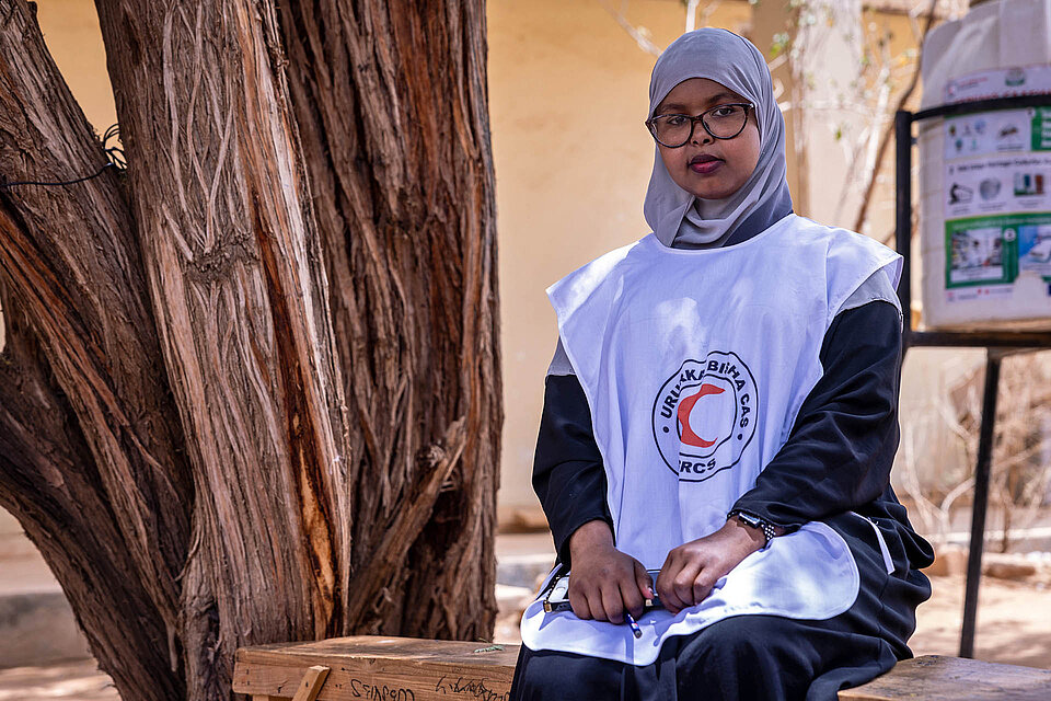 Somalierin mit Rothalbmond-Weste sitzt neben Baum