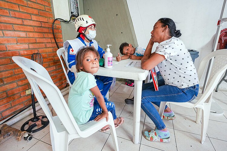 Rotkreuzlerin mit Mutter und 2 Kindern am Tisch