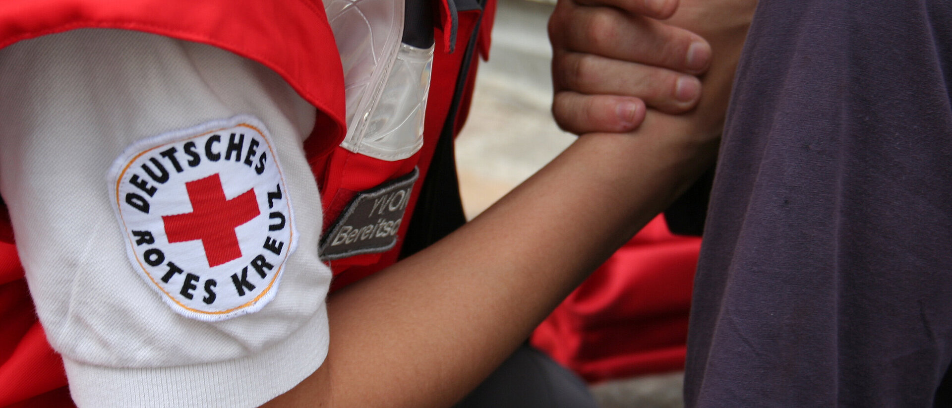 Psychosoziale Notfallversorgung des DRK Ein Mensch mit Rotkreuzabzeichen hält einem anderen Menschen die Hand