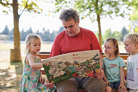 Ein ehrenamtlich Engagierter liest mit Kindern ein Buch.