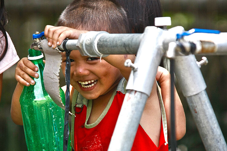 Lachender Junge mit Flasche an Wasserhahn