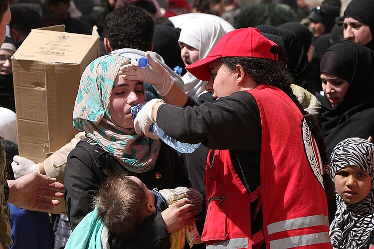 Syrische Helferin gibt einer Frau Wasser