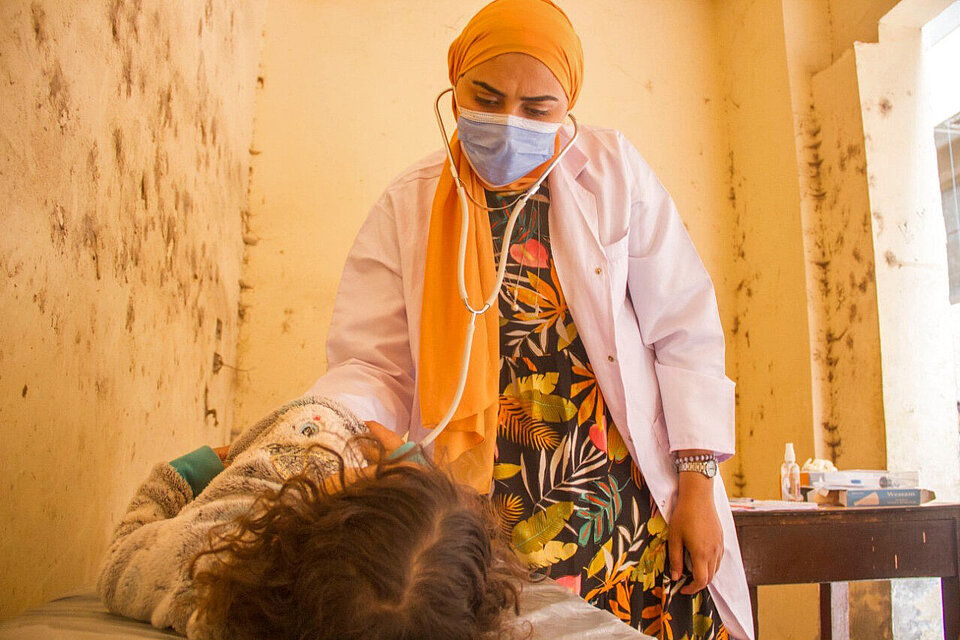 Gesundheitsfürsorge und Einkommenssicherung Ärztin untersucht Kind und Schneiderin zeigt genähtes Kostüm