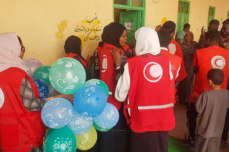 „Freiwillige des SRCS verteilen Ballons und Freude bei einer Veranstaltung für Kinder.“