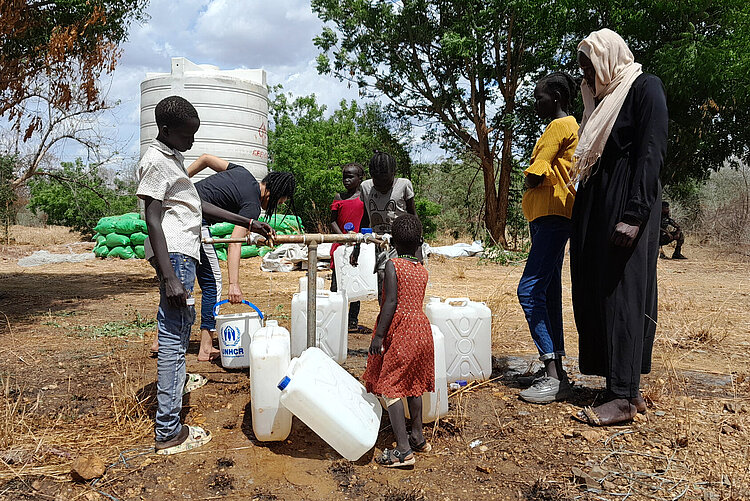 Wash Boll Stiftung Mehrere Personen stehen mit Wasserkanistern um eine Wasserversorgungsstelle