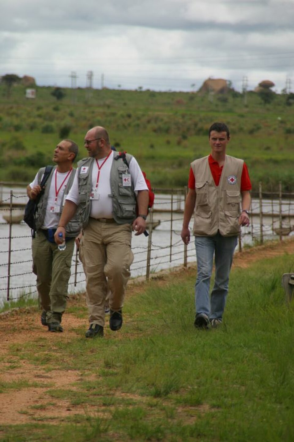 Foto: Drei Mitglieder des Wasserteams des Roten Kreuzes laufen am Ufer einer Wasserquelle entlang.