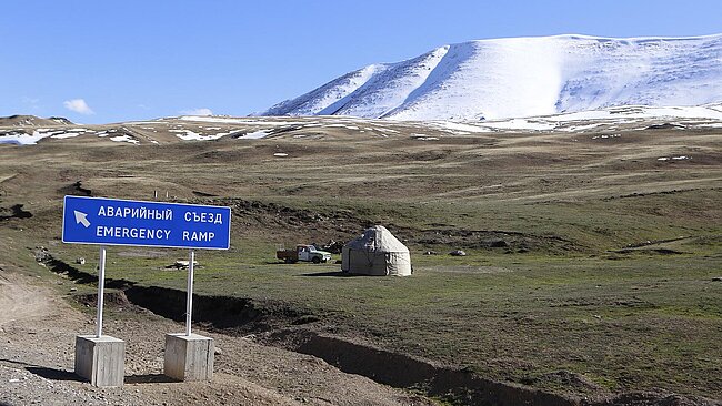 Wiese vor schneebedeckten Bergen und Sicherheitsrampen-Schild