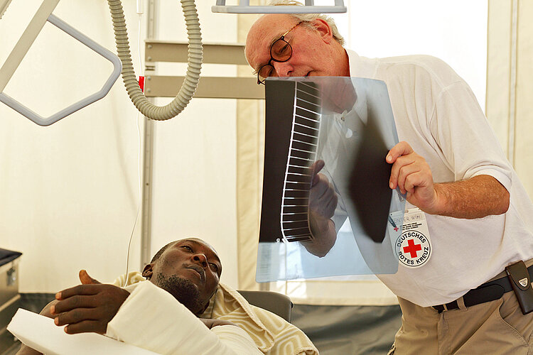 Arzt zeigt liegendem Patienten Röntgenbild