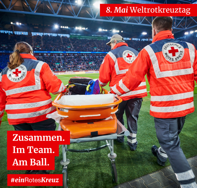 Ein Freiwilliger des Deutschen Roten Kreuzes deutet Anweisungen an einem Fußballfeld an. Text: "8. Mai Weltrotkreuztag. Zusammen. Im Team. Am Ball. #einRotesKreuz."
