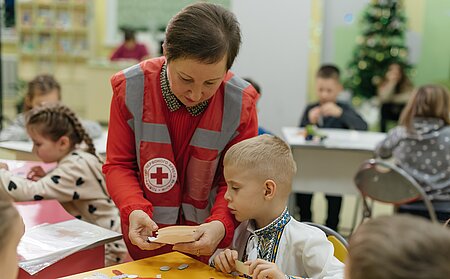 Helfende des Ukrainischen Roten Kreuzes bastelt mit kleinem Kind