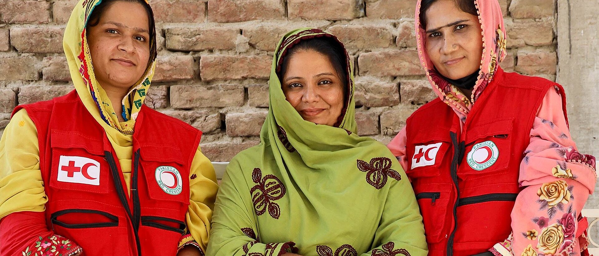 Drei pakistanische Frauen - zwei in Rothalbmond-Kleidung
