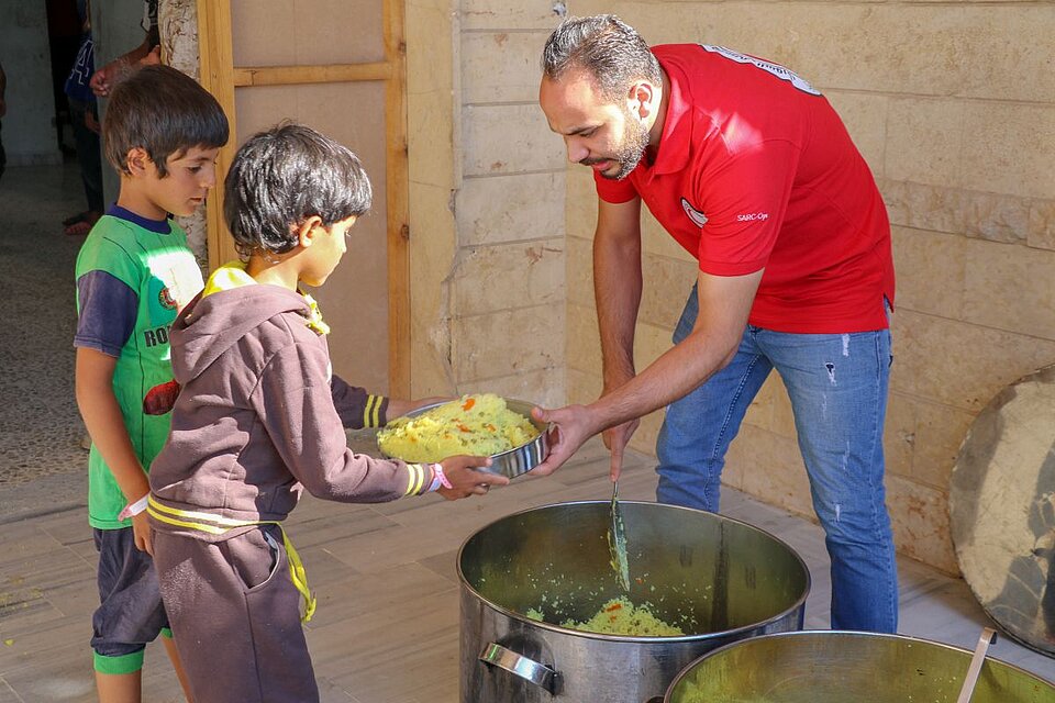 Helfender des Syrischen Arabischen Roten Halbmonds verteilt Nahrung an Kinder